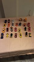 Wide shot of all 26 Hot Wheels cars in rows on a beige tablecloth showing variety of colors and styles