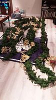 Christmas garland laid out on floor showing gold ribbons, green foliage, and red berries.