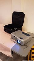 NEC projector powered on with blue light and carrying case open beside it