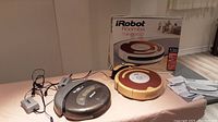 Two iRobot Roomba vacuum cleaners placed on a table with one charger and the Roomba 530 box visible behind.