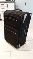 Front and side view of large black Samsonite suitcase standing upright with two front zippered pockets and side handle.
