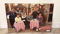 Front view of the plaqued poster showing The Sopranos cast seated and standing around two checkered tables.