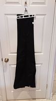 Full length view of black tuxedo pants hanging on door, showing straight leg and unhemmed cuffs.