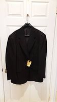Full view of black tuxedo jacket hanging on door, shows overall condition and style.
