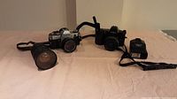 Overview photo showing two vintage film cameras, one zoom lens, and one external flash unit arranged on a surface.