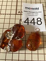 Photo showing both amber pendants on grid background with auction tag for scale