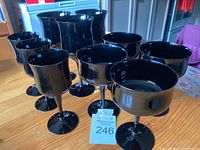 View of ten black glass goblets on a wooden table showing various shapes and a glossy black finish.