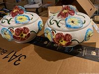 Pair of Italian ceramic cookie jars shown from above and side angles, displaying floral hand-painted decorations with colorful flowers and green vines.