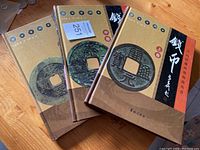 Three hardcover books on Chinese coins stacked on a wooden surface, showing the front covers with ancient cash coin images.
