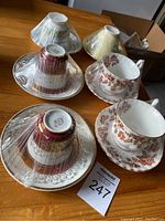 Photo showing all six porcelain tea cups and saucers wrapped in plastic on a wooden surface, highlighting the floral and patterned designs.