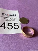 Ring laid flat next to a coin and MaxSold lot number card on purple background