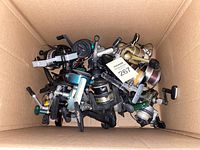 Top-down view of box containing about 15 assorted fishing reels of various colors and designs, showing wear and used condition.