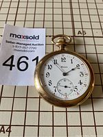 Front view of Illinois pocket watch showing white dial with black Arabic numerals, sub-second dial, and gold-tone case.