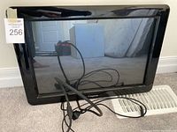 Front view of the Compusa branded karaoke touchscreen TV leaning against a wall with cables visibly attached and coiled on the floor.