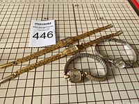 Four vintage ladies watches arranged on a measuring grid, showing two gold-tone linked band watches, a silver-tone expandable band watch, and a silver-tone snake bracelet watch.