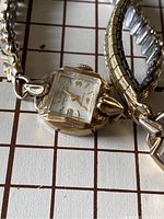 Close-up photo of one ladies mechanical watch showing square dial with numbers and decorative case with silver tone expansion band.