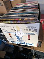 Photo showing a box filled with upright LP vinyl record albums with some visible titles on album covers.