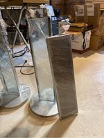 Pair of tall Sony floor speakers wrapped in plastic, showing front and side views with rectangular shape and circular bases.