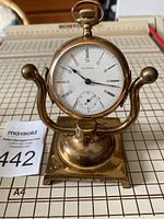 Front view of the Waltham pocket watch mounted on brass stand showing dial and overall appearance