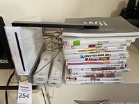 Front view showing white Wii console, two remotes and nunchuks, sensor bar on top, and stack of game cases.