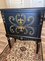 Front view showing black accent chest with two drawers and gold decorative floral motifs