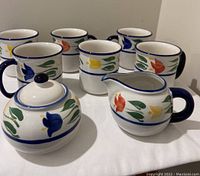 Photo showing all cups, creamer, and sugar bowl with colorful tulip design and blue handles and rims.