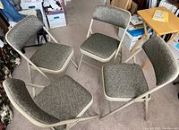 Four beige metal frame folding chairs with padded textured gray fabric seats and backs arranged in a circle on carpet.