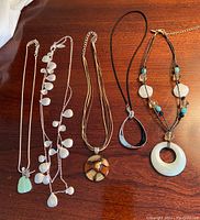 All five necklaces arranged on a wooden surface showing details of pendants and charms.
