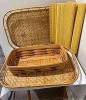 Longaberger basket with two bamboo trays and two rolled woven placemats placed on a white surface.