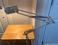 Full side view of the magnifying lamp clamped to a table, showing the flexible double-arm construction with springs for tension.