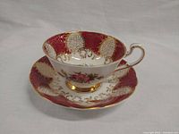 Side view of Paragon teacup placed on matching saucer showing gold filigree, floral motif, and red pattern background.