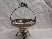 Front angled view of the silver-plated antique dish illustrating intricate floral patterns on the rim and handle, supported by an ornate stand with claw feet.