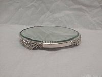 Side view showing the round beveled mirror surface and the silver plated ornate feet raising the tray.