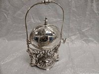 Front view of the silver-plated butter dish with closed spherical lid and upright swing handle.