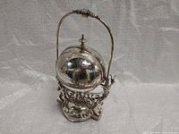 Front perspective view of the antique silver-plated butter dish showing spherical engraved lid, finial, and ornate stand with handle.