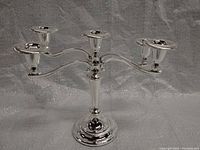 Front side view of the five-arm silver-tone candle stick holder showing the base, central column, and all five curved arms evenly spaced with candle cups.