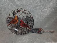 Photo of round ceramic plate with hand-painted cardinals on snowy winter tree branch design, sitting upright with spatula beside it.