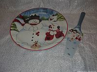Plate and spatula shown side by side on textured gray backdrop, clear winter snowman theme visible on both.
