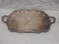 Top-down angled photo of the rectangular tray showing ornate handles, detailed border, and engraved interior with some tarnish.