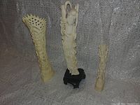 Front view of all three ivory-colored carved figures against silver fabric background