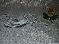 Two clear crystal decorative pieces placed side by side on a glittery surface. Left is a shooting star with pointed facets and three tail streaks; right is a flower pot with yellow flower, green leaves, and clear pot.
