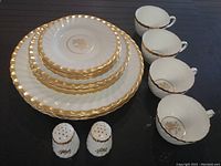 Photo showing stacked dinner and side plates, four tea cups, and salt and pepper shakers