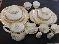 Full set of Minton bone china with rose gold trim including plates, cups, saucers, teapot, sugar and cream dishes, salt and pepper shakers, and serving plates arranged on black surface.