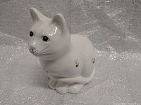 Front facing view of white porcelain cat figurine with pink flower decorations and painted facial details