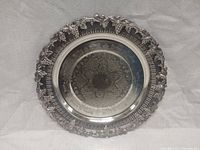 Top view of a round silver plated serving tray featuring an intricate grapevine motif around the edge and etched grape design in the center.
