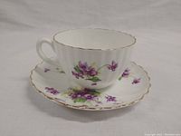 Tea cup and saucer set, showing side view, white china with purple violet floral pattern and gold trim.