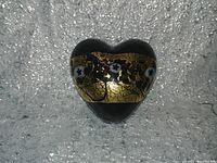 Top view of black heart-shaped art glass with a wide gold foil band decorated with flower motifs.