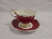 Photo showing teacup resting inside matching saucer highlighting burgundy color and gold trim