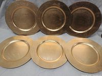 Front view of three gold plastic charger plates standing upright, showing their surface finish and size.