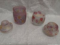Two frosted glass jars with lids, showing colorful abstract designs, one pinkish and one white.